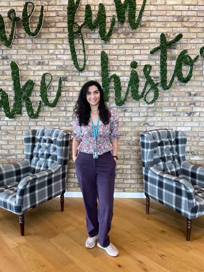 Jamila stands in front of the famous Jeff Bezos quote: “Work hard, have fun, make history.”